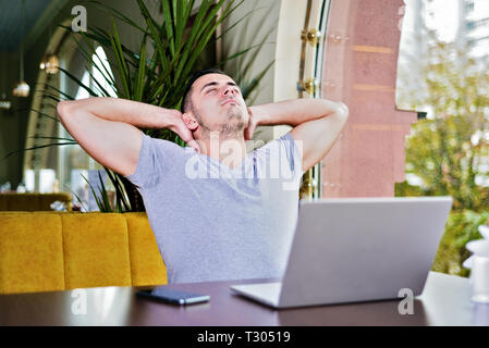 Man with laptop in cafe détend. Un jeune mec avec deux mains tiennent la position et de repos Banque D'Images