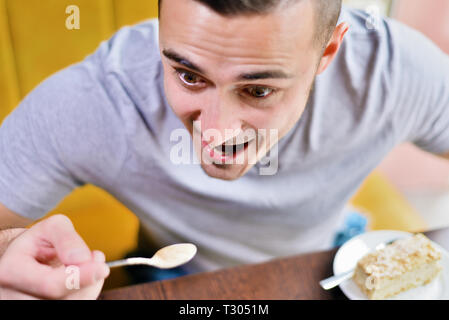 Jeune mec drôle dans le café. homme mange avec une cuillère. sur la table de gâteau soucoupe Banque D'Images