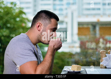 Jeune mec est freelancer dans cafe travailler derrière un ordinateur portable. L'homme de boire du café. Il y a le gâteau sur la table Banque D'Images