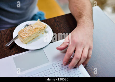 Homme de café à la table contient sa main près de l'ordinateur portable. Il y a du gâteau sur la soucoupe Banque D'Images