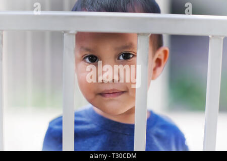 Young hispanic boy derrière les barreaux d'un lit-bébé à la triste au sujet d'obtenir un temps d'arrêt pour mauvaise conduite. Banque D'Images