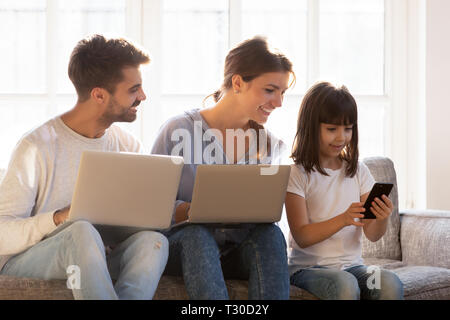 Smiling family sitting on couch absorbée dans appareils numériques Banque D'Images