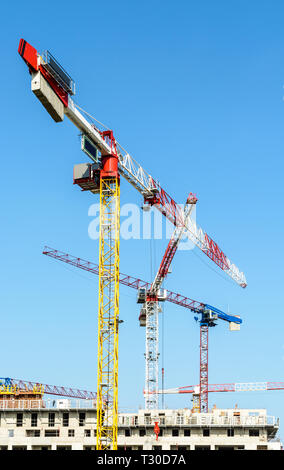 Low angle view of cinq grandes grues à tour au-dessus d'un bâtiment en construction en béton contre le ciel bleu. Banque D'Images