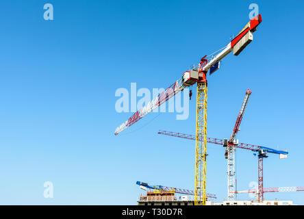 Low angle view of cinq grandes grues à tour au-dessus d'un bâtiment en construction en béton contre le ciel bleu. Banque D'Images