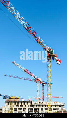 Low angle view of cinq grandes grues à tour au-dessus d'un bâtiment en construction en béton contre le ciel bleu. Banque D'Images