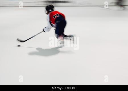 Jeune joueur de hockey en robe rouge avec rondelle en mouvement, mouvement floue sur stade de glace Banque D'Images