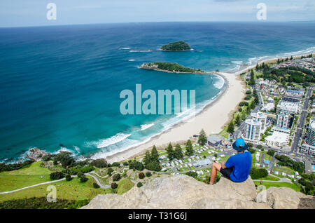 Vue sur la côte depuis le sommet du mont Manganui avec ciel bleu au-dessus et personne en tee-shirt bleu à l'avant-plan, Tauranga, île du Nord, Banque D'Images