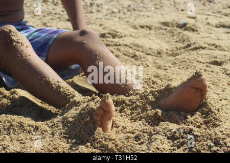 Garçon en short avec jambes partiellement couvert par le sable à la plage Banque D'Images