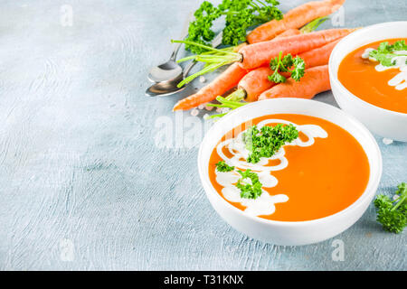 Soupe aux légumes de printemps. Potage à la carotte fait maison, avec des produits bio frais carottes, la crème et les herbes, bleu fond béton copy space Banque D'Images