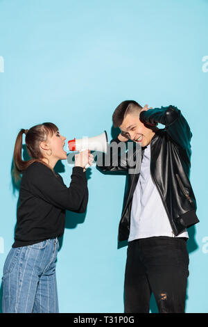 Portrait de jeune fille en denim clothes holding megaphone et crier contre studio bleu arrière-plan. Deux amis de l'adolescence - l'homme et fille avec émotion grave. L'éducation à l'école secondaire concept. Copy space Banque D'Images