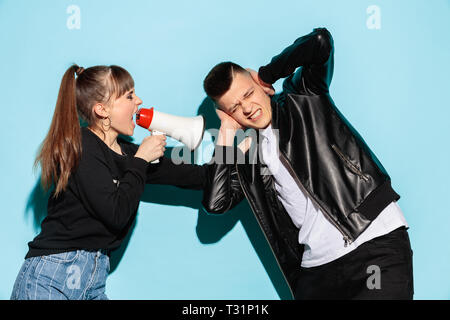 Portrait de jeune fille en denim clothes holding megaphone et crier contre studio bleu arrière-plan. Deux amis de l'adolescence - l'homme et fille avec émotion grave. L'éducation à l'école secondaire concept. Copy space Banque D'Images