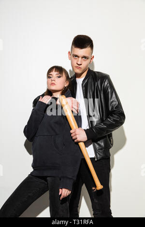 Jeux de sports. Close up fashion portrait de deux jeunes cool hipster girl and boy portant des jeans usés. La femme et l'homme avec un des bâtons de baseball. Studio shot of two cheerful meilleurs amis s'amusant et en faisant des visages. ludique Banque D'Images