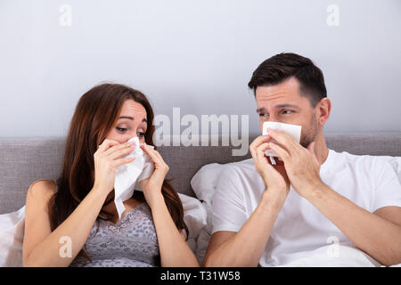 Young Couple Sitting on Bed Blowing leur nez dans la chambre Banque D'Images