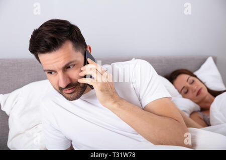 Close-up of Man Talking On Cellphone secrètement pendant que sa femme dort Banque D'Images