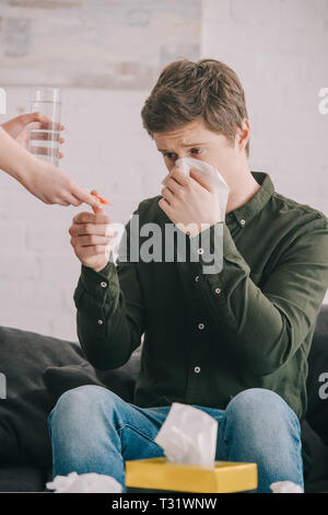 Portrait de femme tenant un verre d'eau et de comprimés près de l'homme l'éternuement dans les tissus Banque D'Images