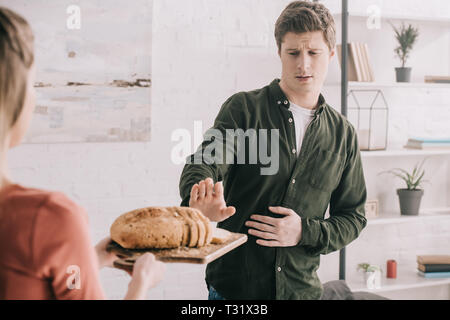 Portrait de femme tenant une planche à découper avec des tranches de pain près de bel homme avec allergie au gluten Banque D'Images