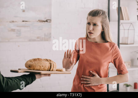 Portrait de l'homme tenue à découper avec du pain près de colère femme blonde avec allergie au gluten Banque D'Images