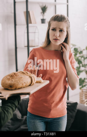 Portrait de l'homme tenue à découper avec du pain près de triste femme blonde avec allergie au gluten Banque D'Images