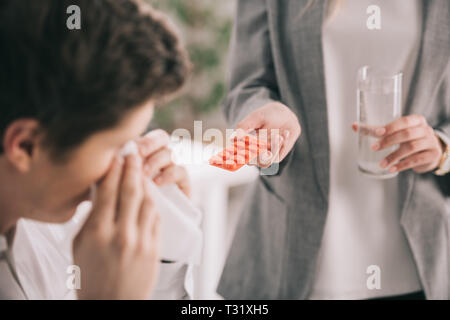 Portrait of woman holding pills et le verre d'eau à proximité de l'éternuement de collaborateur dans les tissus Banque D'Images