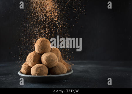 Des boules d'énergie et de truffe au chocolat cacao, noix de coco dans le noir. Poudre de cacao garniture. Des aliments sains pour les enfants et les sucreries vegan, membre suppléant Banque D'Images