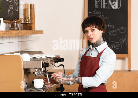 Joli café barista tatoué sur une machine à café et d'looking at camera Banque D'Images