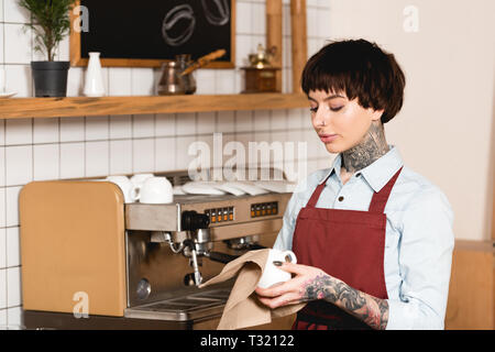 Belle tasse essuyage barista tout en se tenant près de la machine à espresso in coffee shop Banque D'Images