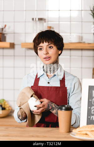 Tablier barista attrayant en coupe d'essuyage en position debout près de comptoir bar Banque D'Images