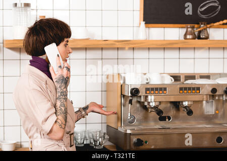 Surpris businesswoman talking on smartphone tout en se tenant près de la machine à expresso Banque D'Images