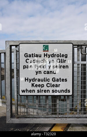 Porte en acier galvanisé avec multilingue anglais et gallois avertissement, gates hydraulique garder clairement quand retentit la sirène, Galles du nord port de Caernarfon Banque D'Images