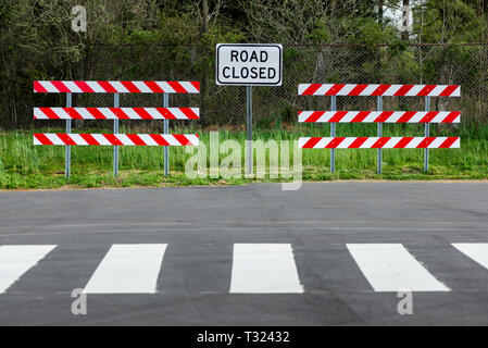 De l'horizontale rouge et blanc à rayures avec des obstacles d'une route signe clos au milieu d'eux. Il y a une zone boisée derrière eux. Banque D'Images