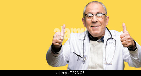 Beau médecin senior homme portant un manteau de l'approbation médicale faisant geste positif avec la main, les pouces jusqu'en souriant et heureux pour le succès. Regardant le ca Banque D'Images