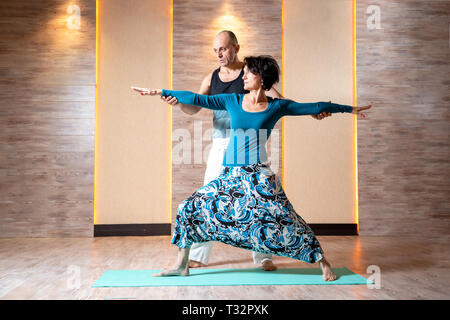 Homme et femme brune adultes pratiquent le yoga en se tenant sur le tapis bleu dans la salle de sport. Banque D'Images