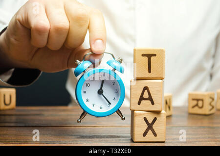 Businessman's hand holding une horloge près de la blocs en bois avec le mot taxe. Le temps de payer des impôts. Le concept d'imposition annuelle. Les taxes sur les véhicules, pro Banque D'Images