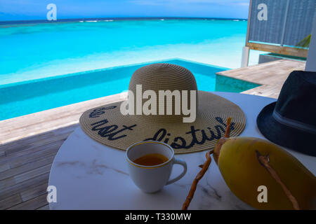 Tasse de café sur une table avec une noix de coco et deux chapeaux avec une étiquette Ne pas déranger dans une Beach pool villa dans l'île de Kuramathi, Maldives. Banque D'Images