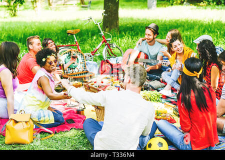 Groupe d'amis appréciant un pique-nique tout en mangeant et buvant du vin rouge assis sur une couverture dans un parc en plein air - Les jeunes ont un drôle de rencontre Banque D'Images