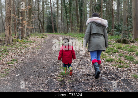 La mère et l'enfant de deux ans bien marcher dans les bois portant des wellies shot de derrière Banque D'Images