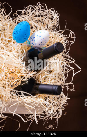 Deux bouteilles de vin rouge et blanc et bleu deux oeufs dans le fort avec de la paille. Concepts de Pâques avec des cadeaux sur fond jaune paille. Banque D'Images