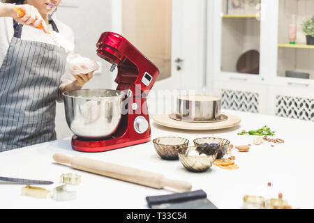 Jeune femme pâtissier bat la crème dans un bol en métal rouge dans un mélangeur électrique. Le concept de pâtisserie maison, la cuisine Banque D'Images