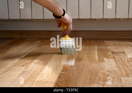 Parquet vernis laquage par paintbrush - deuxième couche. Accueil rénovation de parquet. Coups de pinceau de vernis sur un parquet en bois. Application Banque D'Images