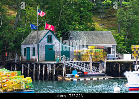Des drapeaux américains et nautiques voler sur une petite cabane de pêche construit sur un quai empilé avec des casiers à homard. New Harbor, Maine, USA. Banque D'Images