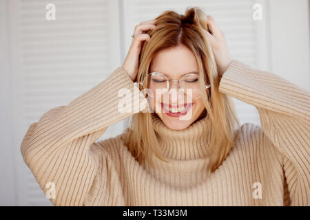 Belle et élégante jeune blonde avec des lunettes et beige pull oversize. Jeune femme portant des croisillons et smiling Banque D'Images