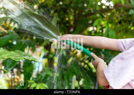 Les enfants sont l'arrosage des plantes avec un flexible en caoutchouc dans le jardin. Banque D'Images