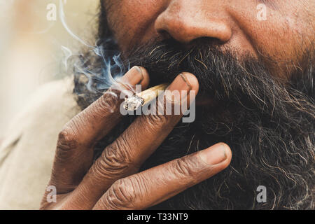Hindu sadhu Fumeurs ganja, la marihuana avec chillum sur les ghats du Gange à Varanasi, Inde . Close up. Inhaler la fumée d'une cigarette. Mauvaise h Banque D'Images