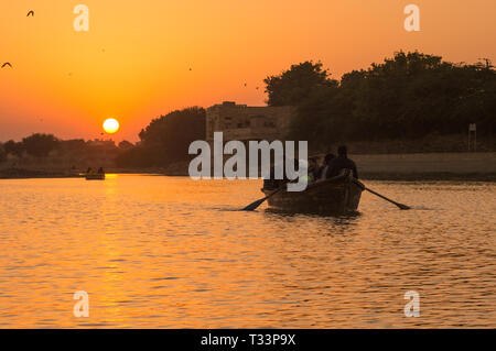 Les personnes qui prennent un tour de bateau sur le lac Gadi Sagar à Jaisalmer au coucher du soleil avec le soleil en arrière-plan Banque D'Images