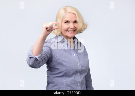 Belle senior woman smiling et montrant des signes de petite taille avec des doigts. mesurer le concept Banque D'Images