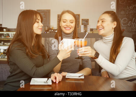 Trois copines se réunissent dans le café. Boire des boissons et parler les uns les autres. Vue de face. Banque D'Images