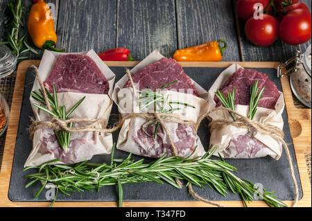 Steaks de viande crue et de romarin. La viande fraîche sur une planche à découper, d'Herbes et légumes Banque D'Images