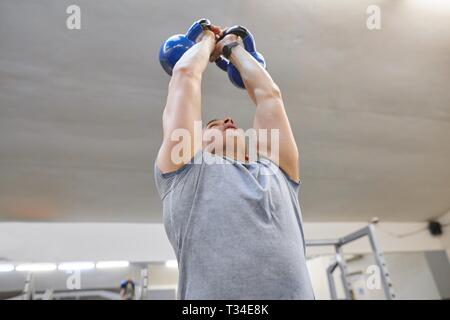 L'exercice de l'homme sportif musculaire très fort avec kettlebells dans une salle de sport, la formation de poids. Banque D'Images