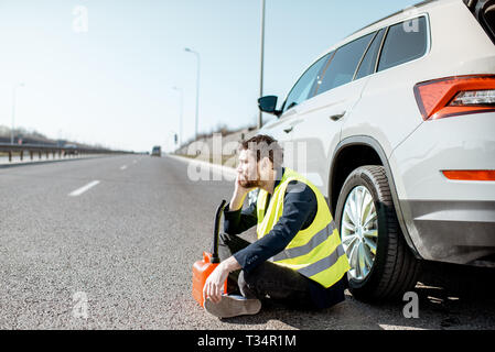 Homme avec désespoir émotions assis avec le plein de sa voiture près de la cartouche sur le bord de la route Banque D'Images