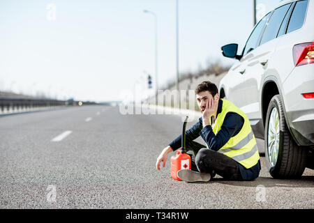 Homme avec désespoir émotions assis avec le plein de sa voiture près de la cartouche sur le bord de la route Banque D'Images